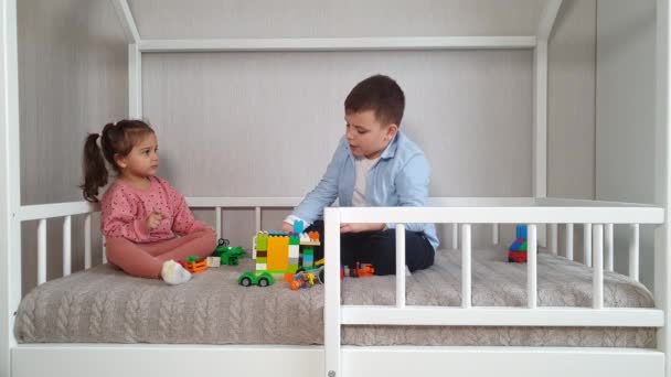 2人の子供の弟と妹がモンテッソーリベッドに座っておもちゃのレンガで遊んでいます — ストック動画
