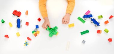 Oyuncak uçak ve beyaz arka planda oyuncak tuğlalarla oynayan çocuk ellerini kapat. Metnin için boşluk kopyala.