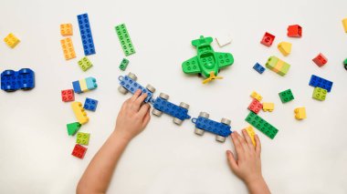 Beyaz arka planda oyuncak tuğlalarla oynayan çocuk ellerini kapat. Metnin için boşluk kopyala.