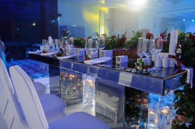 Düğün resepsiyonu parti masası. Kırmızı şakayık ve güllerle süslenmiş şarap kadehleri. Çatal ve bıçaklar.