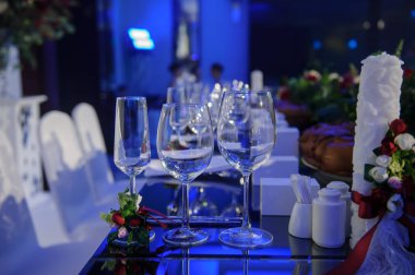 Düğün resepsiyonu parti masası. Kırmızı şakayık ve güllerle süslenmiş şarap kadehleri. Çatal ve bıçaklar.