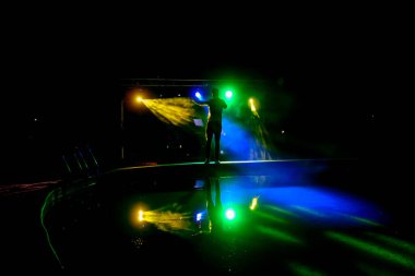 Sahnede bir şarkıcının karanlık siluetiyle havuz partisi. Parlak çok renkli ışıkları olan bir arka plan. Bir müzik grubu konseri.