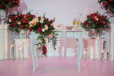 Düğün fotoğrafı standı kırmızı şakayık ve güllerle süslenmiş. Beyaz vazoda çiçekler. Şeffaf gözlüklerdeki mumlar