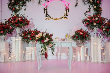 Düğün fotoğrafı standı kırmızı şakayık ve güllerle süslenmiş. Beyaz vazoda çiçekler. Şeffaf gözlüklerdeki mumlar