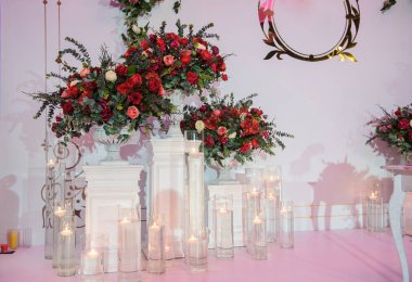 Düğün fotoğrafı standı kırmızı şakayık ve güllerle süslenmiş. Beyaz vazoda çiçekler. Şeffaf gözlüklerdeki mumlar