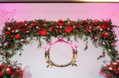 Düğün fotoğrafı standı kırmızı şakayık ve güllerle süslenmiş. Beyaz vazoda çiçekler. Şeffaf gözlüklerdeki mumlar