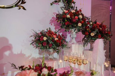 Düğün fotoğrafı standı kırmızı şakayık ve güllerle süslenmiş. Beyaz vazoda çiçekler. Şeffaf gözlüklerdeki mumlar