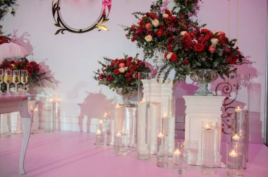 Düğün fotoğrafı standı kırmızı şakayık ve güllerle süslenmiş. Beyaz vazoda çiçekler. Şeffaf gözlüklerdeki mumlar