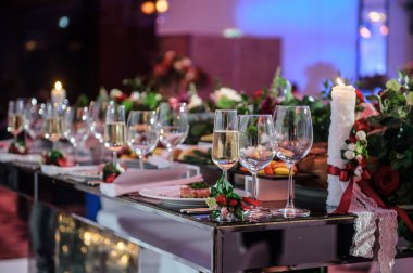 Düğün resepsiyonu parti masası. Kırmızı şakayık ve güllerle süslenmiş şarap kadehleri. Çatal ve bıçaklar.