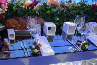 Düğün resepsiyonu parti masası. Kırmızı şakayık ve güllerle süslenmiş şarap kadehleri. Çatal ve bıçaklar.