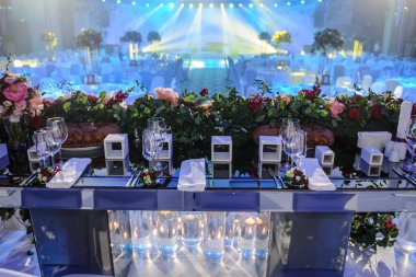 Düğün resepsiyonu parti masası. Kırmızı şakayık ve güllerle süslenmiş şarap kadehleri. Çatal ve bıçaklar.