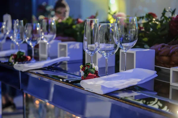 Düğün resepsiyonu parti masası. Kırmızı şakayık ve güllerle süslenmiş şarap kadehleri. Çatal ve bıçaklar.
