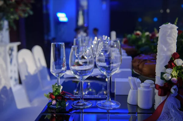 Düğün resepsiyonu parti masası. Kırmızı şakayık ve güllerle süslenmiş şarap kadehleri. Çatal ve bıçaklar.