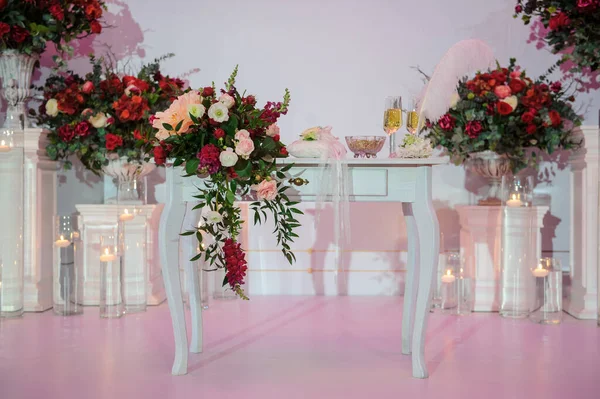 Düğün fotoğrafı standı kırmızı şakayık ve güllerle süslenmiş. Beyaz vazoda çiçekler. Şeffaf gözlüklerdeki mumlar