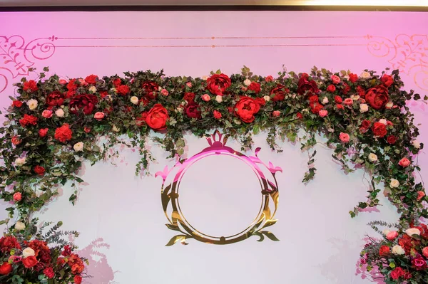 Düğün fotoğrafı standı kırmızı şakayık ve güllerle süslenmiş. Beyaz vazoda çiçekler. Şeffaf gözlüklerdeki mumlar