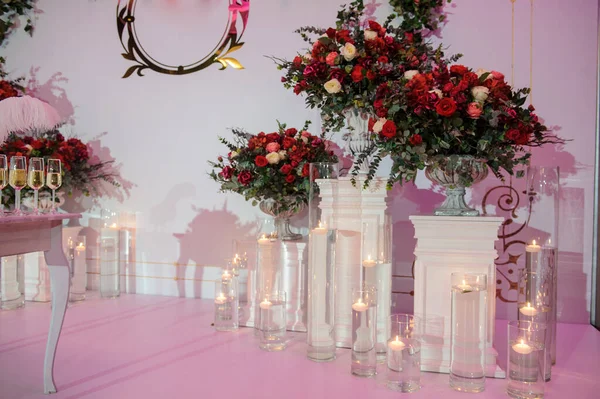 Düğün fotoğrafı standı kırmızı şakayık ve güllerle süslenmiş. Beyaz vazoda çiçekler. Şeffaf gözlüklerdeki mumlar