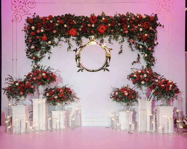 Düğün fotoğrafı standı kırmızı şakayık ve güllerle süslenmiş. Beyaz vazoda çiçekler. Şeffaf gözlüklerdeki mumlar