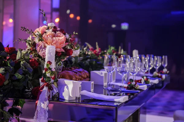 Düğün resepsiyonu parti masası. Kırmızı şakayık ve güllerle süslenmiş şarap kadehleri. Çatal ve bıçaklar.