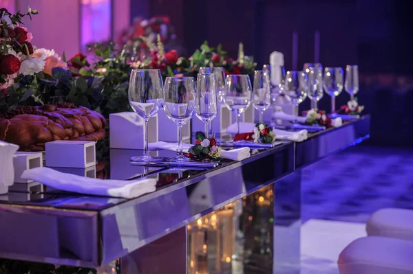 Düğün resepsiyonu parti masası. Kırmızı şakayık ve güllerle süslenmiş şarap kadehleri. Çatal ve bıçaklar.