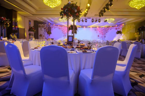 Düğün resepsiyonu parti masası. Kırmızı şakayık ve güllerle süslenmiş şarap kadehleri. Çatallar, bıçaklar, tabaklar