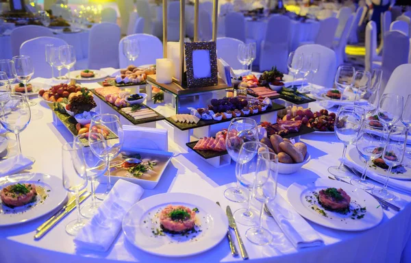 Düğün resepsiyonu parti masası. Kırmızı şakayık ve güllerle süslenmiş şarap kadehleri. Çatallar, bıçaklar, tabaklar