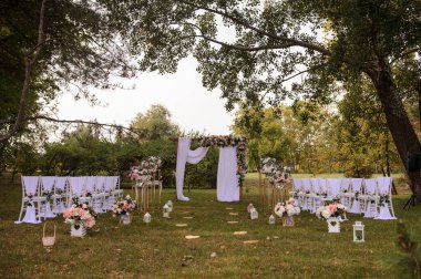 Park / Orman 'da bir düğün hazırlığı. Ahşap kemer ve sandalyeler beyaz ve pembe çiçeklerle süslenir güller ve şakayıklar, yerde mumlarla süslenir..  