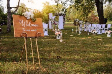 Park / Orman 'da bir düğün hazırlığı. Tahtaya hoş geldin tahtası ve sandalyeler beyaz ve pembe çiçeklerle süslenir. Güller ve şakayıklar, yerde mumlarla süslenir..