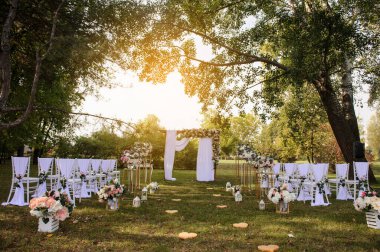 Park / Orman 'da bir düğün hazırlığı. Ahşap kemer ve sandalyeler beyaz ve pembe çiçeklerle süslenir güller ve şakayıklar, yerde mumlarla süslenir..  