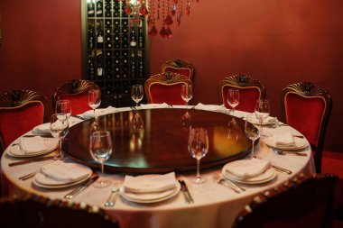 Kırmızı duvarları olan eski şarap imalathanesinde. Tabak bıçaklı, çatallı, peçeteli ve şarap kadehli beyaz masa.