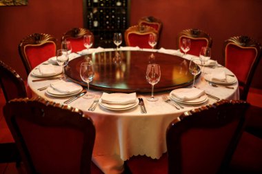 Kırmızı duvarları olan eski şarap imalathanesinde. Tabak bıçaklı, çatallı, peçeteli ve şarap kadehli beyaz masa.