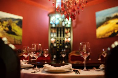 Kırmızı duvarları olan eski şarap imalathanesinde. Tabak bıçaklı, çatallı, peçeteli ve şarap kadehli beyaz masa.