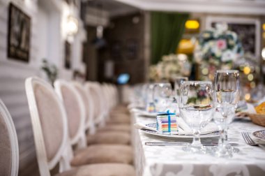 Eski bir restoranın düğün resepsiyonunu kapatın. Masanın üzerinde mavi kurdele, şarap kadehi, bıçak, çatal ve peçeteyle bağlanmış küçük çikolatalar var.