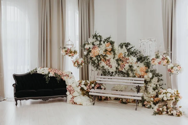 Vintage wedding party photo booth zone in studio, decorated with black sofa and white wood bench under the flowers