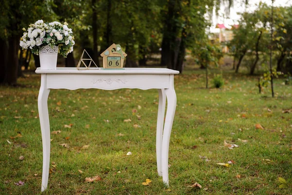 Üzerinde çiçekler olan beyaz ahşap masa, düğün dekorasyonunun bir parçası.