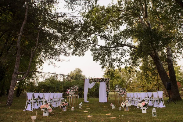 Park / Orman 'da bir düğün hazırlığı. Ahşap kemer ve sandalyeler beyaz ve pembe çiçeklerle süslenir güller ve şakayıklar, yerde mumlarla süslenir..  