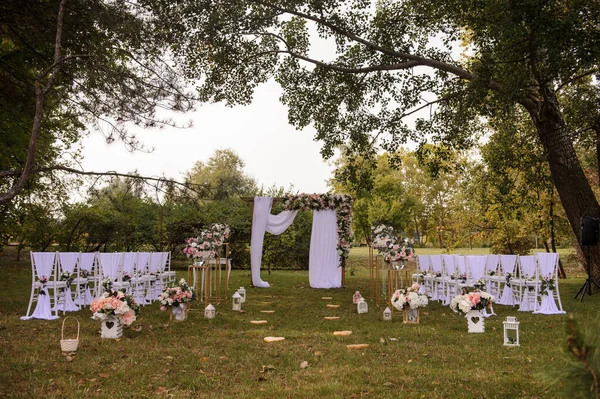 Park / Orman 'da bir düğün hazırlığı. Ahşap kemer ve sandalyeler beyaz ve pembe çiçeklerle süslenir güller ve şakayıklar, yerde mumlarla süslenir..  