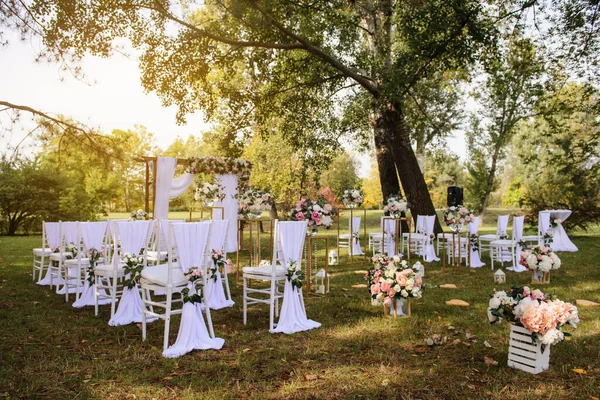 Park / Orman 'da bir düğün hazırlığı. Ahşap kemer ve sandalyeler beyaz ve pembe çiçeklerle süslenir güller ve şakayıklar, yerde mumlarla süslenir..  