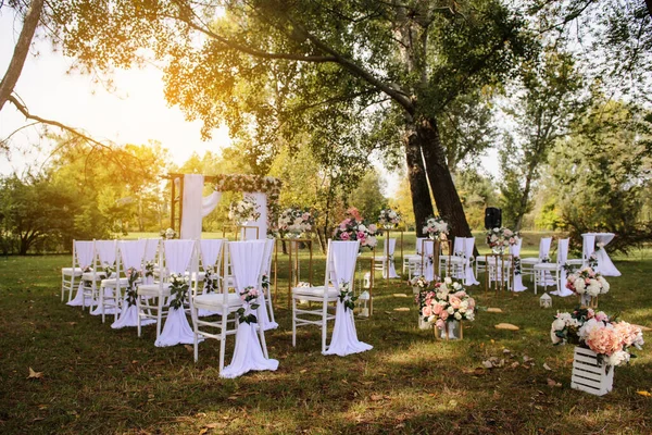 Park / Orman 'da bir düğün hazırlığı. Ahşap kemer ve sandalyeler beyaz ve pembe çiçeklerle süslenir güller ve şakayıklar, yerde mumlarla süslenir..  