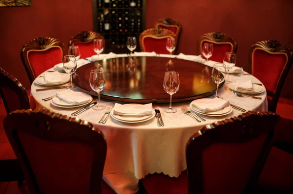 Kırmızı duvarları olan eski şarap imalathanesinde. Tabak bıçaklı, çatallı, peçeteli ve şarap kadehli beyaz masa.