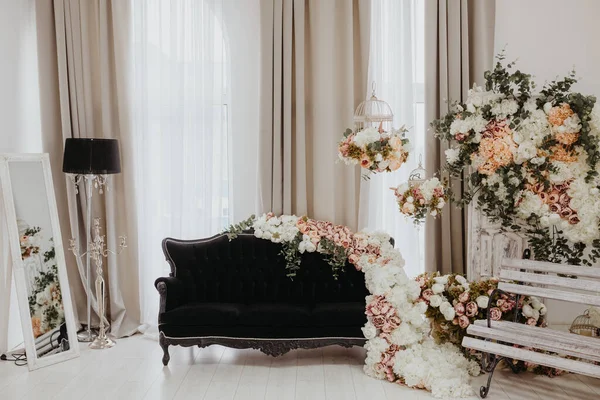 スタジオのヴィンテージウェディングパーティーフォトブースゾーンは 花の下に黒いソファと白い木のベンチで飾られています ロイヤリティフリーのストック写真