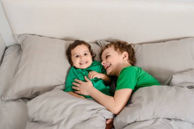 Mutlu küçük çocuklar yatakta yeşil tişörtlü kız ve erkek kardeşler gülümsüyor, gülüyorlar. Çocuklar gezegen kavramını kurtaracak.