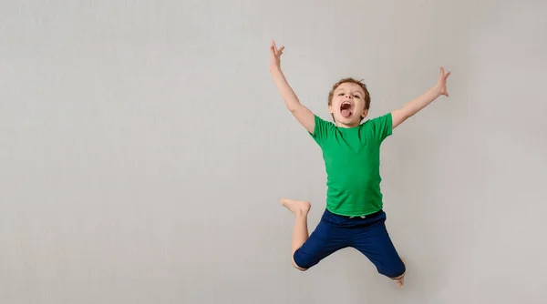 灰色の背景に緑のTシャツの幸せな小さな子供の男の子 笑ってジャンプ笑顔です 子供たちは地球の概念を救うでしょう テキストとロゴのための無料スペース ストック写真