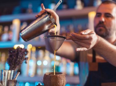 Barmen çubukta hindistan cevizi kabuğunda süzgeç kullanarak meyve suyu dolduruyor.