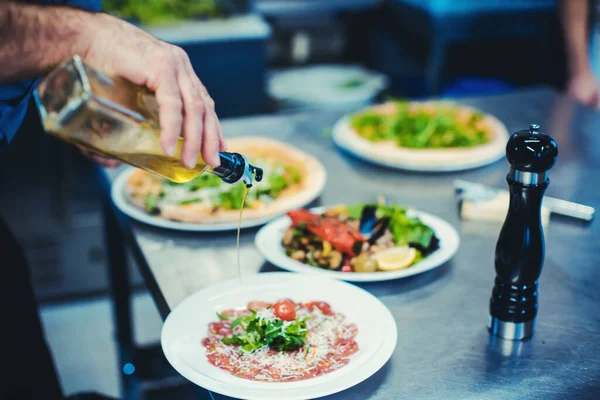 Chef finishing meals in restaurant kitchen with olive oil — Stock Photo, Image