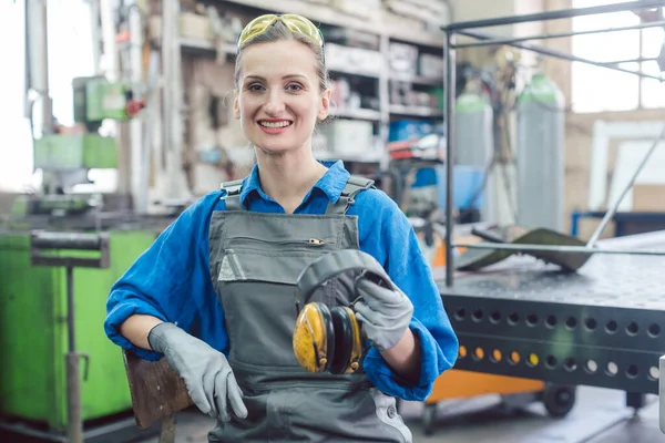 Lavoratrice in fabbrica di metallo che mostra abbigliamento da lavoro protettivo — Foto Stock