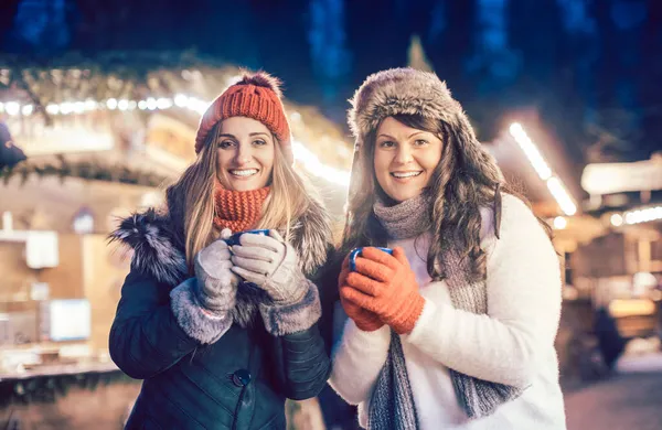 Zwei Frauen mit heißem Glühwein vor Weihnachtsmarktstand — Stockfoto