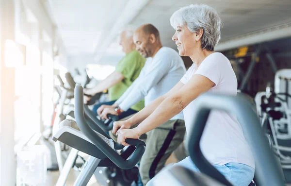 Fit senioren op stationaire fitness fietsen in de sportschool — Stockfoto