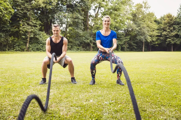 Young man and woman exercising using battle rope — Stock Photo, Image