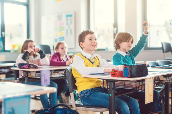 Pupils in elementary school class raising hands to answer — Stock Photo, Image