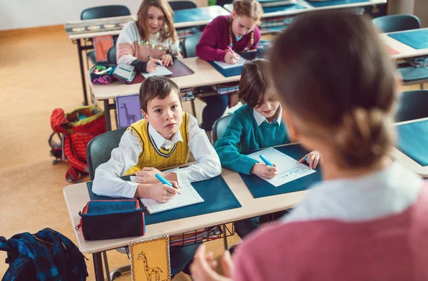 Öğrenciler, oğlanlar ve kızlar, sınıfta öğretmenlerini dinliyorlar.